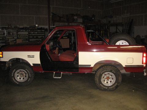 1991 Ford Bronco - The side profile of a two-tone 1991 Ford Bronco is visible, with its interior and spare tire in the cargo area.