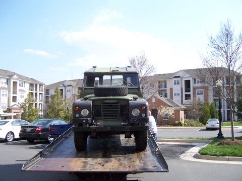 1974 Land Rover Land Rover - This Land Rover is being transported on a flatbed truck, with apartment buildings in the background. The registry indicates it is a 1974 mo…