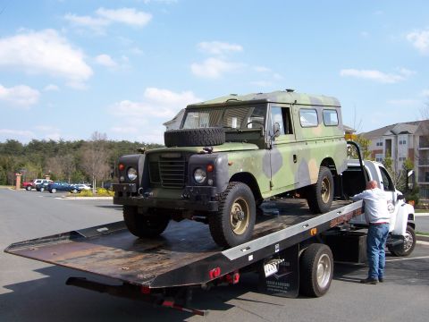 1974 Land Rover Land Rover - A camouflaged Land Rover Defender is loaded onto a flatbed tow truck.