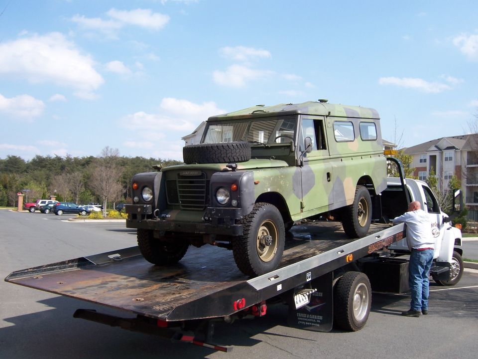 Camouflage Land Rover Series hardtop loaded on a tilted flatbed tow truck