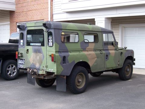 1974 Land Rover Land Rover - This camouflaged Land Rover is parked next to a black SUV in front of a garage.