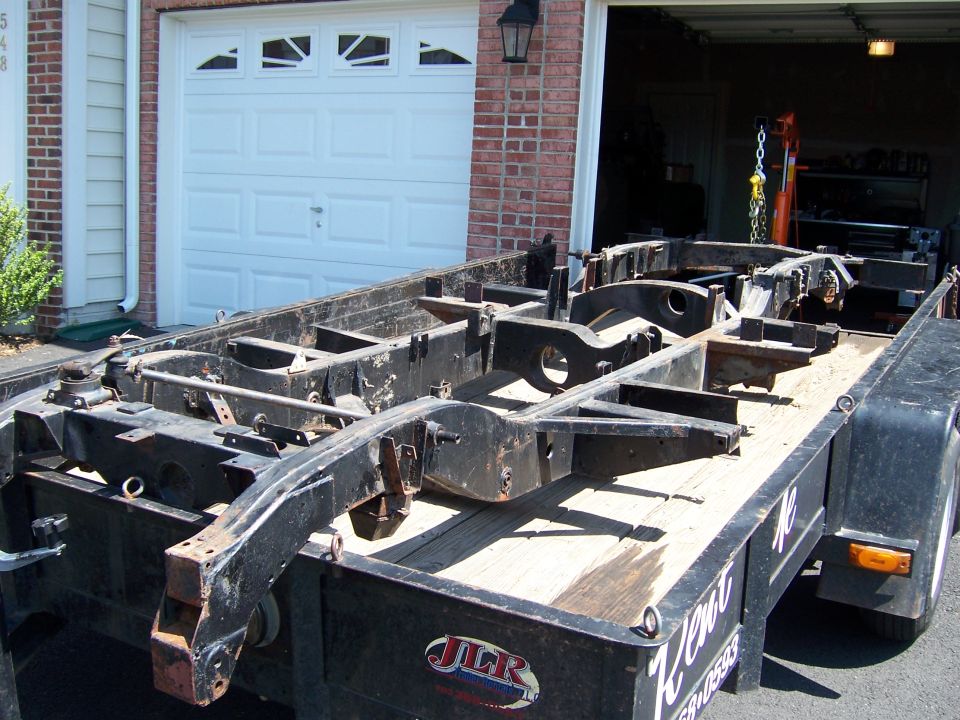 Bare truck frame loaded on a trailer in front of a garage