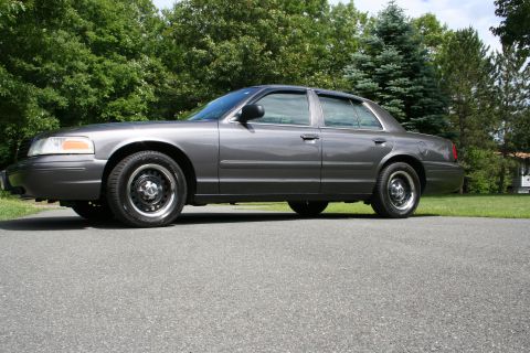 2000 Ford Crown Victoria - Side profile of a gray 2000 Ford Crown Victoria sedan parked on an asphalt surface with trees in the background.