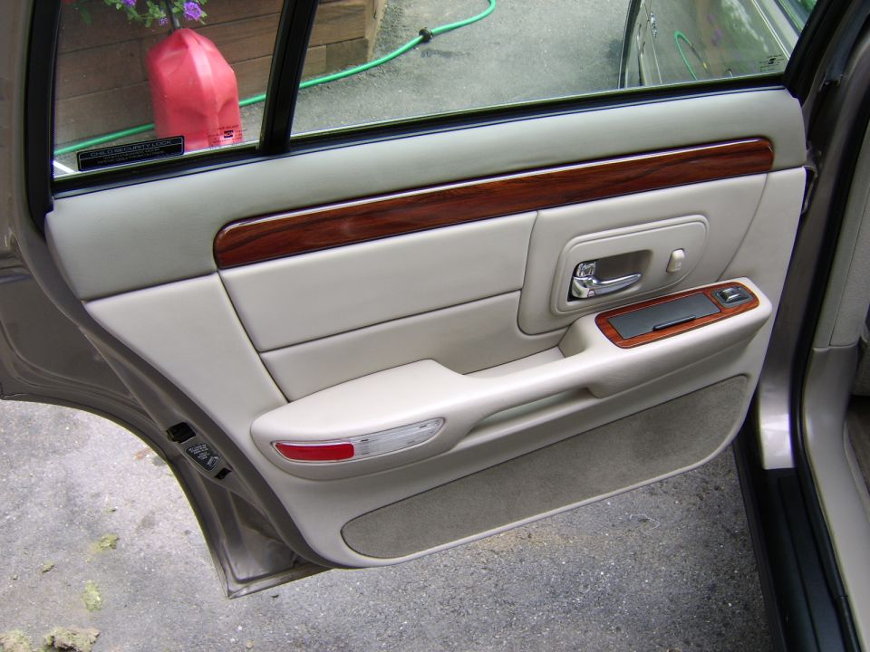 Tan rear car door panel interior with wood trim and chrome handle