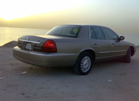 2007 Mercury Grand Marquis - Rear view of a 2007 Mercury Grand Marquis sedan parked on a sandy area near the ocean.