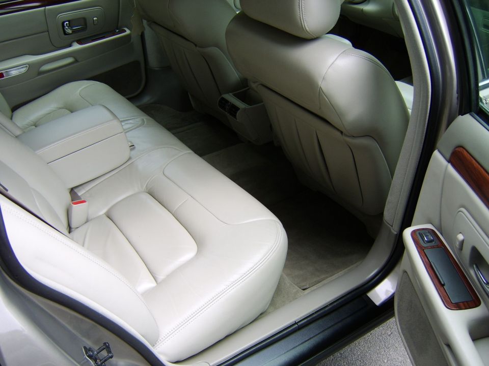 Beige leather rear seat interior of a sedan with open door and woodgrain trim
