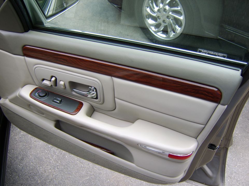 Beige leather car door panel with wood trim and chrome switches