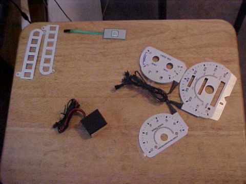 1995 Ford Taurus - Various automotive gauge faces and electronic components are arranged on a table, likely for installation or repair.