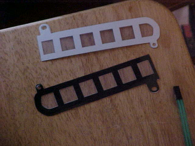 Two metal strips with square cutouts, one white and one black, lie on a wooden surface