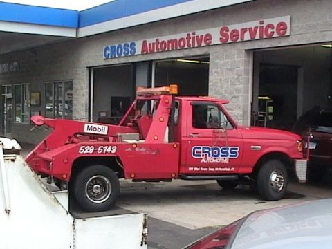 1990 Ford Bronco - A red tow truck is parked outside a garage with "CROSS Automotive Service" visible on the building.