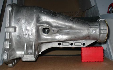 1999 Ford Crown Victoria - Side profile of a bare cast aluminum transmission extension housing sitting on cardboard, showing the mounting flange at left, a raised cas…
