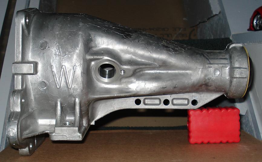 Side view of bare aluminum transmission extension housing with cast W marking on a bench