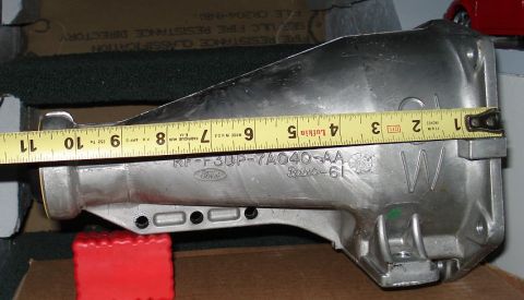 1999 Ford Crown Victoria - Cast aluminum transmission extension housing lying on cardboard with a yellow Lufkin tape measure stretched along its length, reading rough…