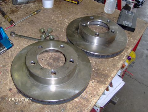 1978 Ford Bronco - Two brake rotors and associated hardware are laid out on a workbench, likely for installation or comparison.