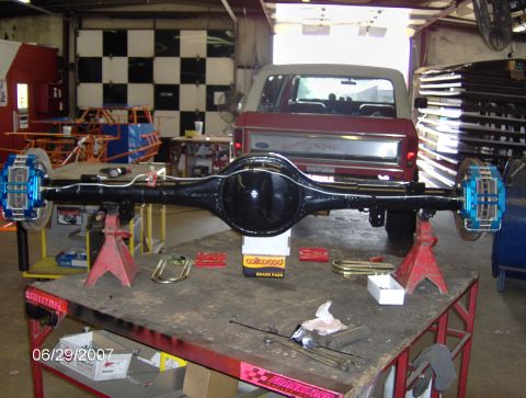 1978 Ford Bronco - Rear axle assembly with disc brakes, with a red Ford Bronco visible in the background.