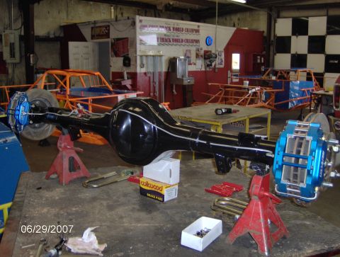 1978 Ford Bronco - Rear axle assembly with disc brakes, race car chassis visible in workshop.