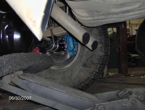 1978 Ford Bronco - Close-up of a vehicle's rear axle and brake system, showing a blue caliper and dual exhaust pipes.