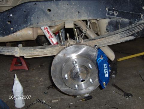 1978 Ford Bronco - Close-up of a blue GRUB disc brake caliper being installed on a vehicle's rear rotor, with Rancho RS 5000 shock absorber visible.