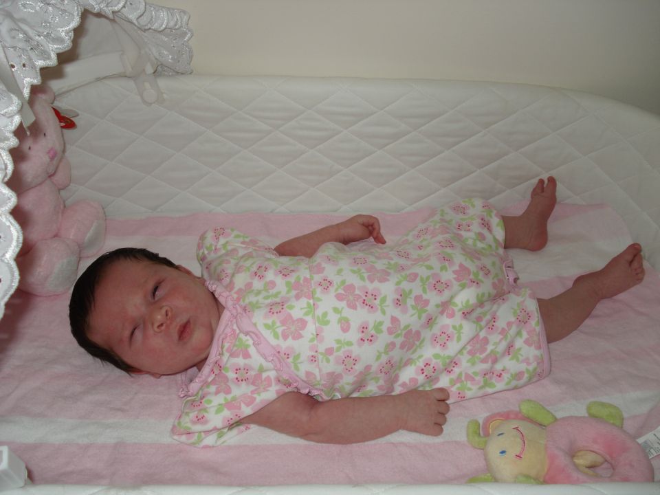 Newborn baby in a floral-print outfit lying on a pink and white striped blanket in a crib
