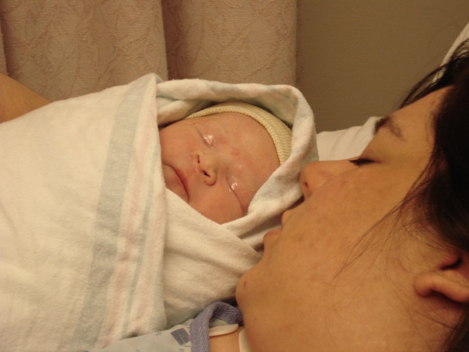 Newborn baby wrapped in a blanket, eyes closed, looking at mother