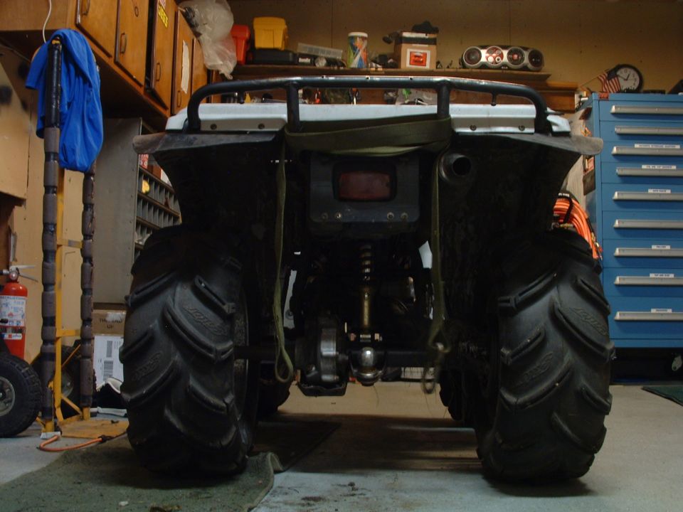 Rear view of an ATV with large mud tires and a hitch ball, parked in a garage
