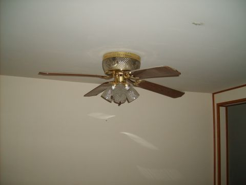 2004 Ford Crown Victoria - A ceiling fan with wooden blades and glass light fixtures is mounted on a white ceiling. The fan has a gold-colored base and trim.