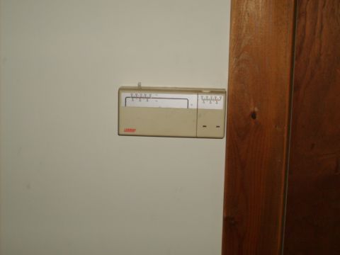 2004 Ford Crown Victoria - A beige thermostat is mounted on a light-colored wall next to a wooden door frame.