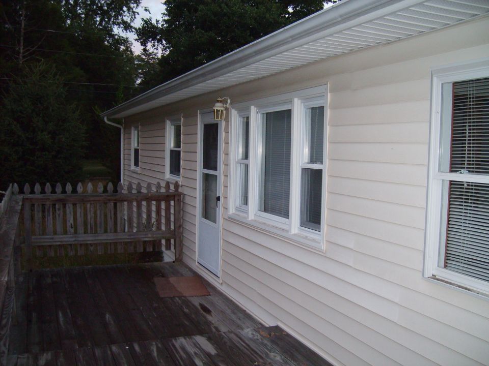 Exterior of a house with a wooden deck and railing. A door and several windows are visible