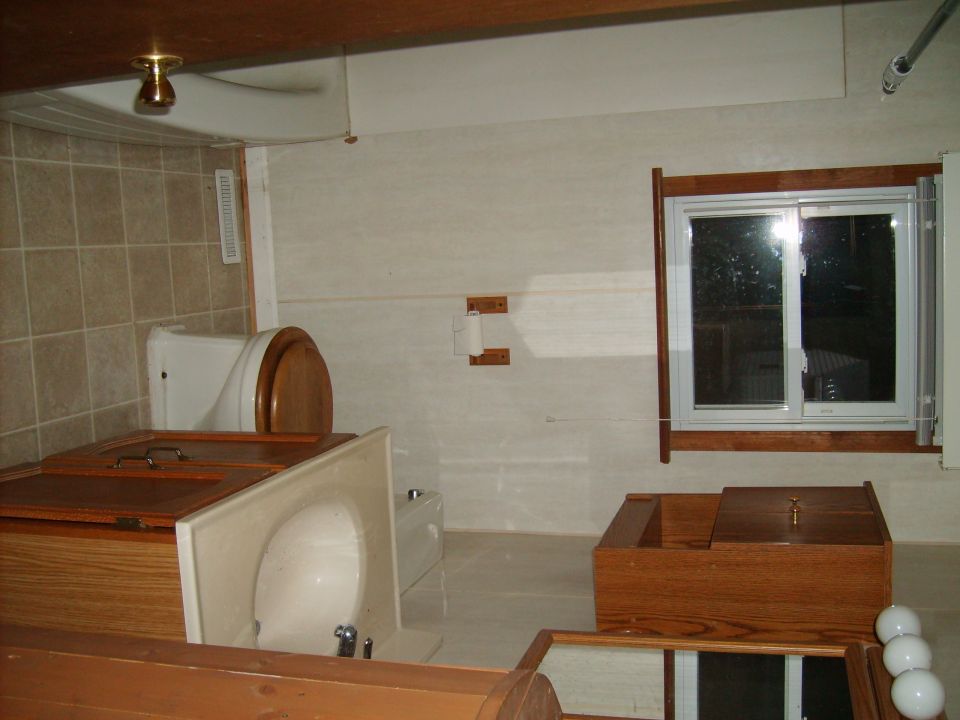 Bathroom with toilet, sink, and wooden cabinets. Window shows outside view