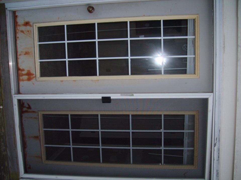 Exterior view of a double door with two sets of windows; the top window has a cream-colored frame, the bottom has a wood-tone frame
