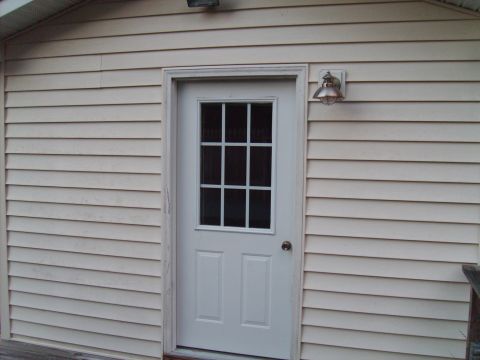 2004 Ford Crown Victoria - A white door with a glass pane is mounted on a beige vinyl-sided wall, with a light fixture overhead.