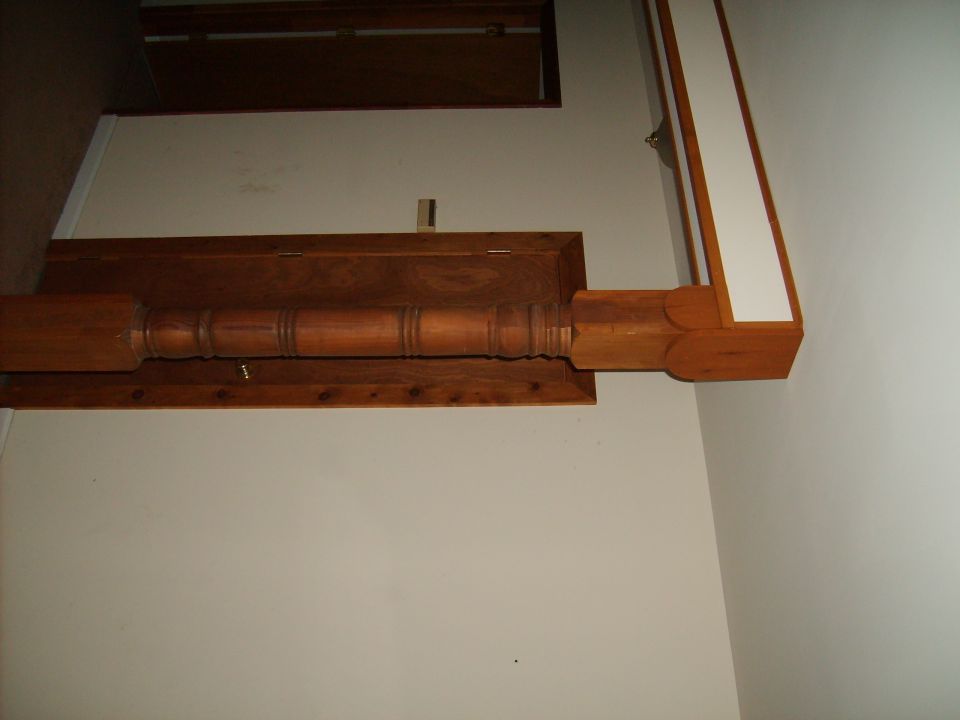 Wooden staircase newel post and handrail against white wall