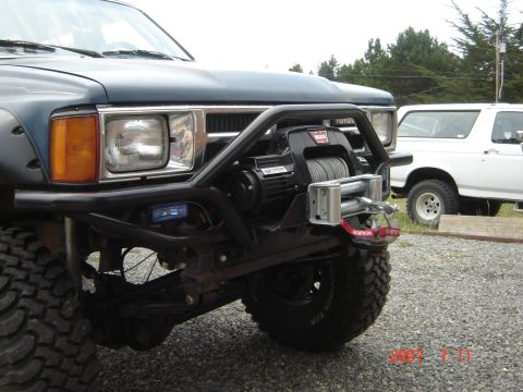 1993 Ford Bronco - Front view of a modified dark blue Toyota pickup truck with a winch, parked next to a white Ford Bronco.