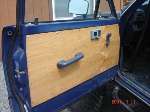 1993 Ford Bronco - Interior view of a blue vehicle, custom wood door paneling and a gray interior handle.