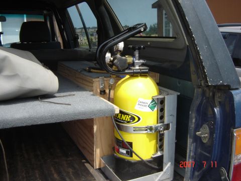 1993 Ford Bronco - A yellow carbon dioxide tank is mounted inside a vehicle, next to custom wooden shelving and a gray carpeted surface.