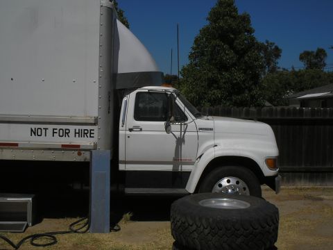 1999 Ford F-800 - A white box truck is parked next to a large cargo trailer. The truck's cab is visible from the front three-quarter view.