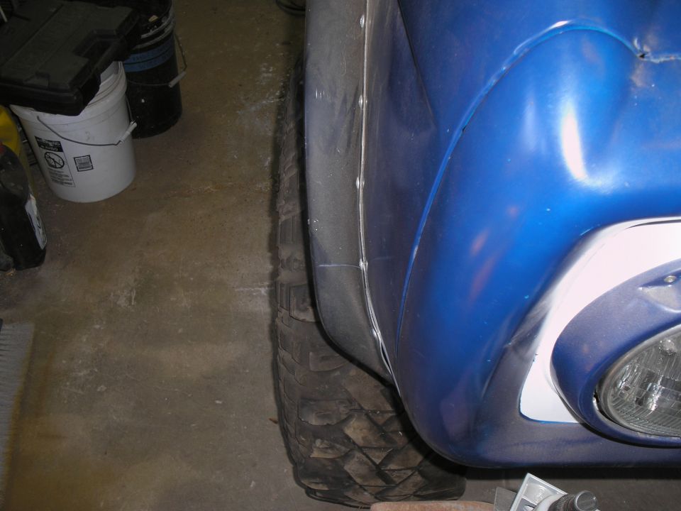 Close-up of a blue vehicle's fender and off-road tire. Supermotors.net logo visible