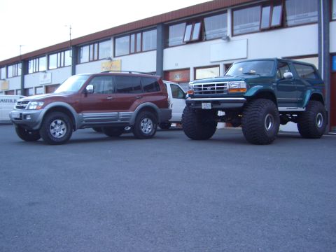 1996 Ford Bronco - A modified green Ford Bronco with massive tires sits parked in front of a commercial building.