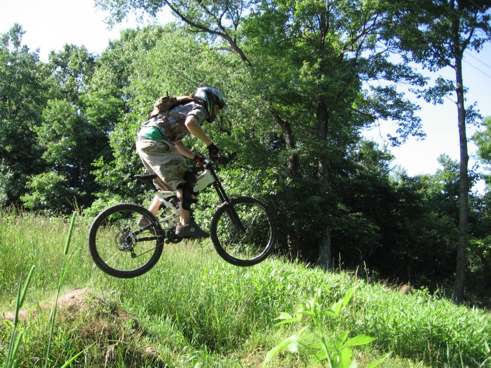 Mountain biker mid-air over grassy terrain, trees in background
