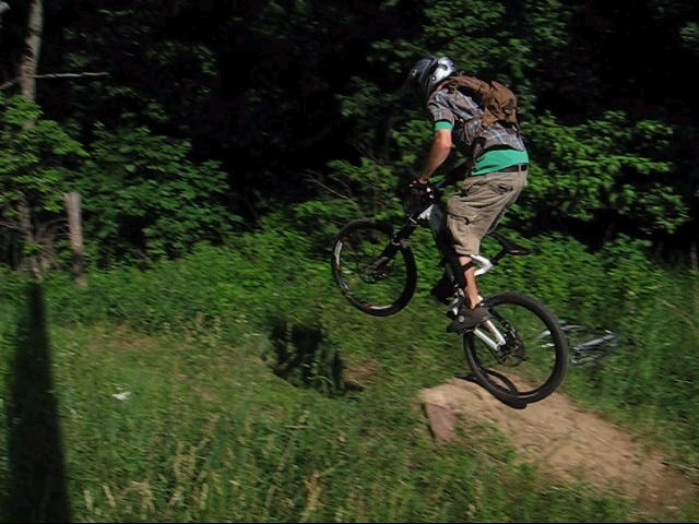 Mountain biker mid-air over a dirt jump, wearing a helmet and backpack