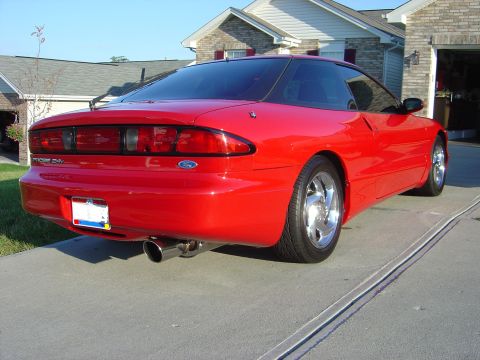 1997 Ford Probe - The rear view of a red 1997 Ford Probe shows its taillights, exhaust, and a portion of the garage and house.