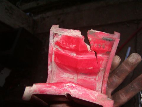 1991 Ford Bronco - A close-up view of a broken red plastic component covered in white dust, revealing stamped numbers.