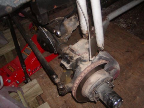 1991 Ford Bronco - Close-up view of a vehicle's front axle and suspension system, supported by a red hydraulic jack.