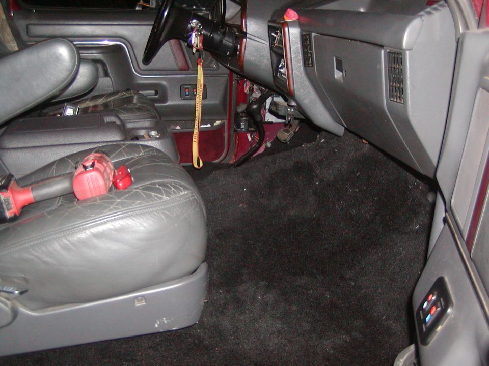 Interior shot of a vehicle's passenger side, showing cracked leather seat, black carpet, and dashboard with steering wheel and center console