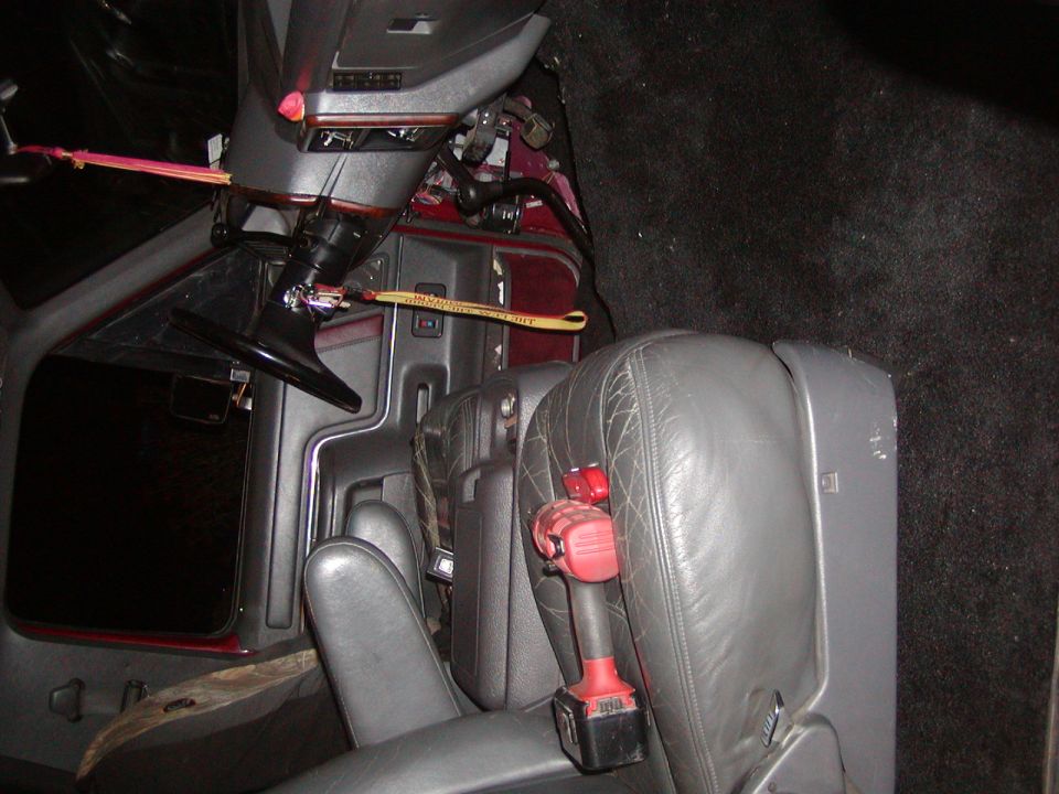 Vehicle interior showing seats, steering wheel, and a drill resting on the passenger seat
