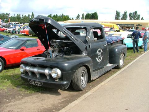 2001 Ford Fiesta - A modified black pickup truck from the 1950s is displayed with its hood open, revealing a powerful engine.