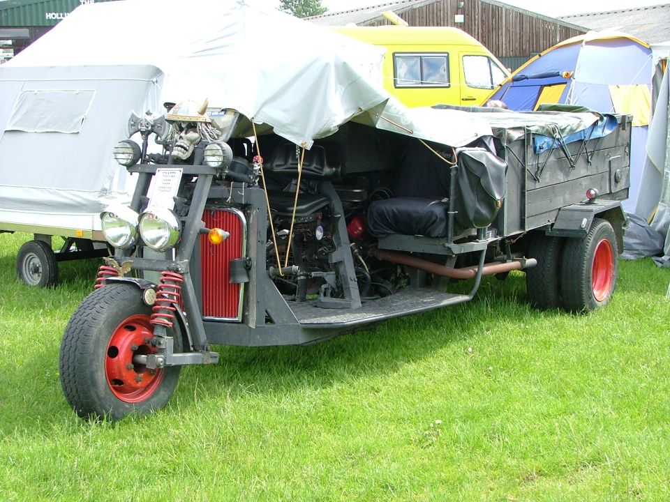 Custom trike with a skull and axes on the front, a tent over the top, and a trailer attached