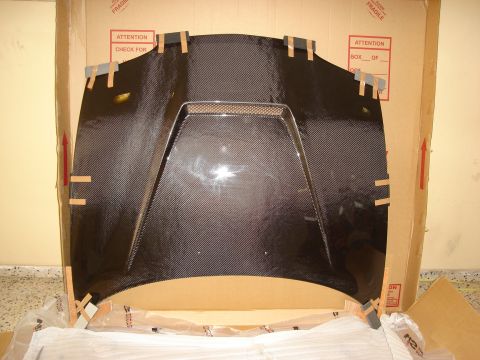 1995 Mazda MX-6 - A carbon fiber car hood is shown inside its shipping box, secured with tape.