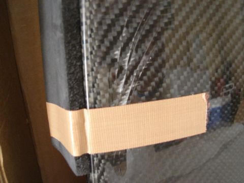 1995 Mazda MX-6 - A close-up of a carbon fiber panel, partially wrapped in plastic and taped, with a SuperMotors logo visible.