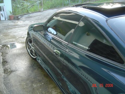 1995 Mazda MX-6 - A dark green coupe with chrome rims is parked on a wet concrete surface.